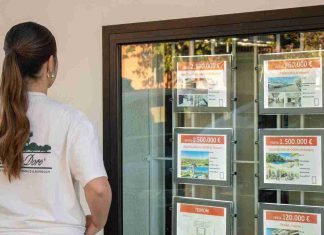 Una mujer joven observa los anuncios de viviendas en el escaparate de una inmobiliaria en Madrid, donde se muestran precios de venta superiores al millón de euros.